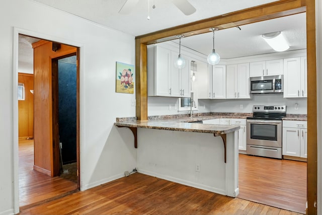 kitchen with kitchen peninsula, appliances with stainless steel finishes, white cabinets, and a breakfast bar area