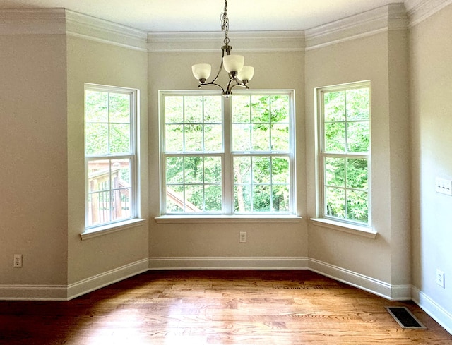 unfurnished room with plenty of natural light, an inviting chandelier, ornamental molding, and hardwood / wood-style flooring