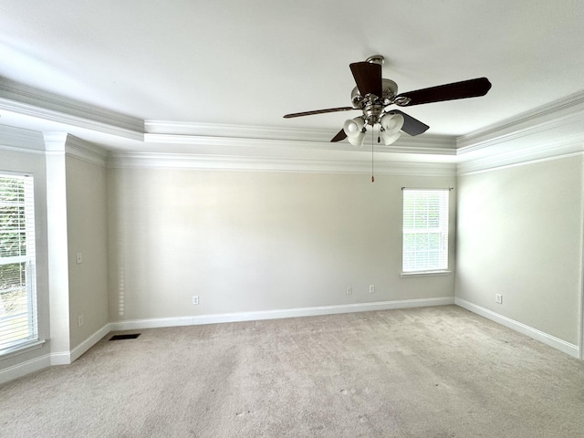 carpeted spare room with a tray ceiling, ceiling fan, a healthy amount of sunlight, and ornamental molding