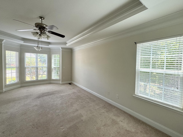 carpeted empty room with a tray ceiling, crown molding, ceiling fan, and a healthy amount of sunlight