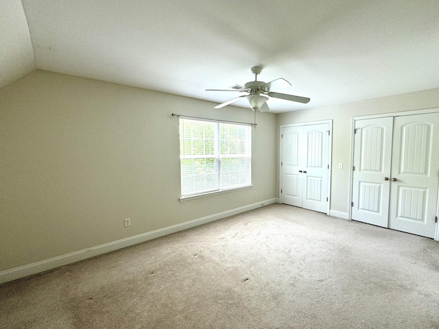 unfurnished bedroom with ceiling fan, lofted ceiling, light carpet, and multiple closets