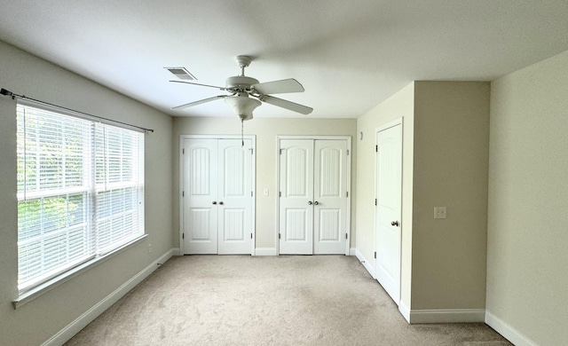 unfurnished bedroom with light colored carpet, ceiling fan, and multiple closets