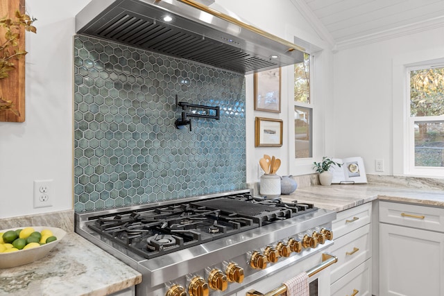 kitchen featuring lofted ceiling, light stone counters, white cabinets, wall chimney exhaust hood, and stainless steel stove