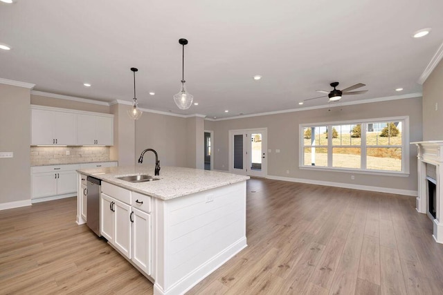 kitchen with sink, white cabinetry, hanging light fixtures, light stone counters, and a center island with sink