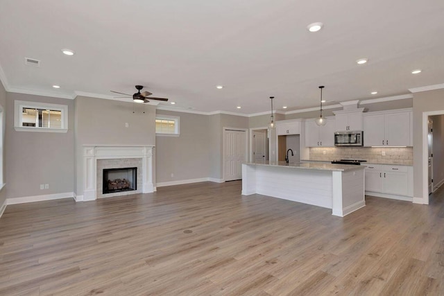 kitchen with pendant lighting, tasteful backsplash, light hardwood / wood-style floors, an island with sink, and white cabinets