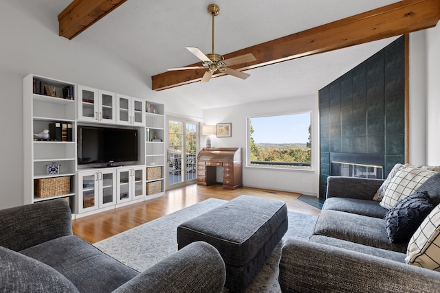 living room featuring french doors, vaulted ceiling with beams, a fireplace, ceiling fan, and light wood-type flooring