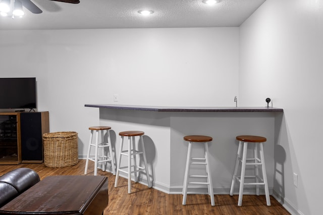 bar with a ceiling fan, a textured ceiling, wood finished floors, baseboards, and bar area