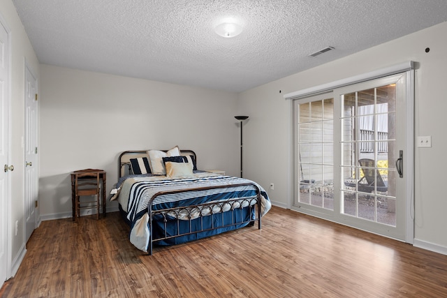 bedroom featuring a textured ceiling, access to exterior, visible vents, wood finished floors, and baseboards