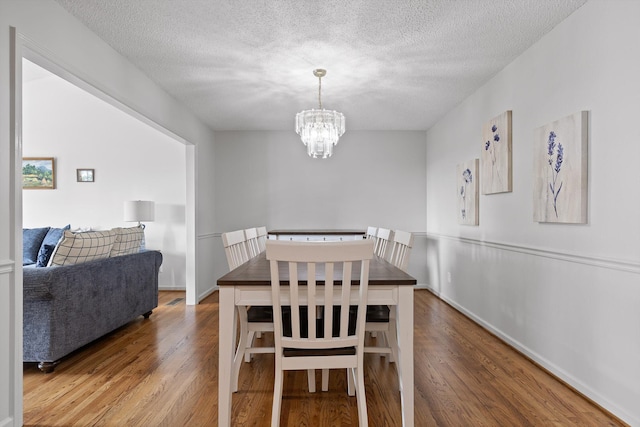 dining space with baseboards, a textured ceiling, wood finished floors, and a notable chandelier