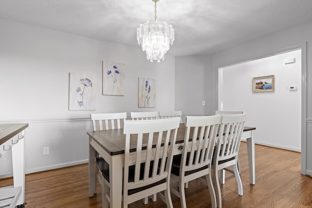 dining room with baseboards, a textured ceiling, a notable chandelier, and wood finished floors
