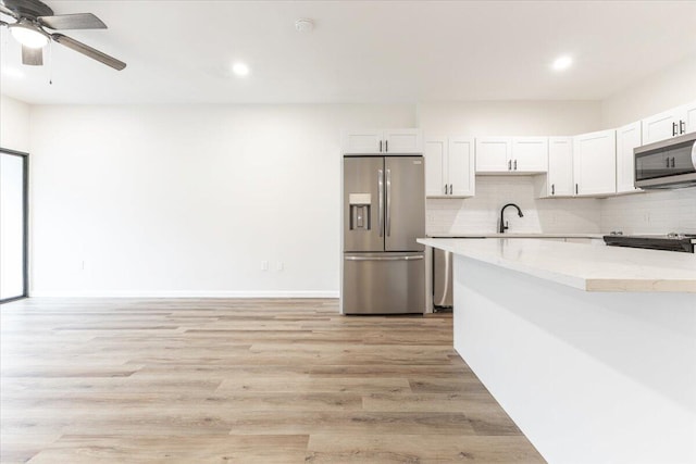 kitchen with white cabinets, decorative backsplash, appliances with stainless steel finishes, and light hardwood / wood-style flooring