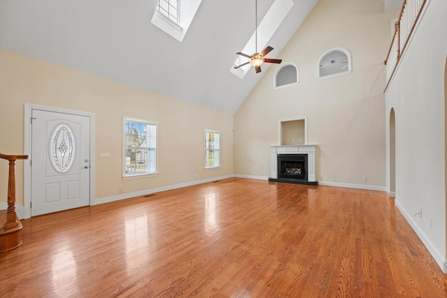 unfurnished living room featuring light hardwood / wood-style floors, high vaulted ceiling, a skylight, and ceiling fan