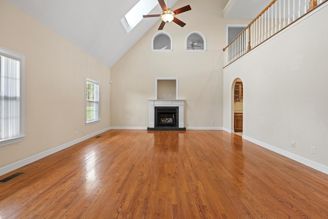 unfurnished living room featuring hardwood / wood-style floors, ceiling fan, high vaulted ceiling, and a skylight