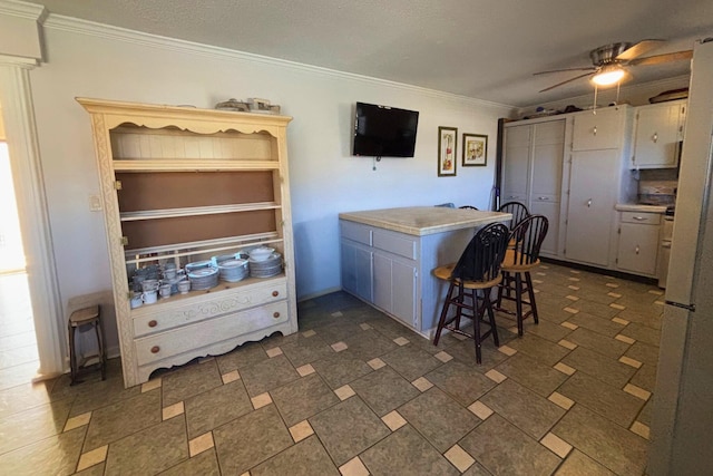 kitchen with a peninsula, ceiling fan, a kitchen breakfast bar, and crown molding