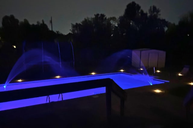 pool at night featuring a storage unit and an outdoor pool