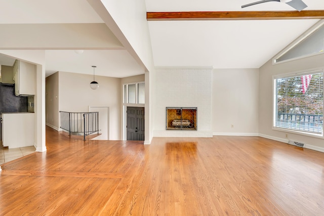 unfurnished living room featuring a fireplace, ceiling fan, vaulted ceiling with beams, and light hardwood / wood-style flooring