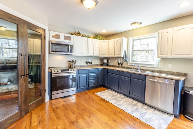 kitchen featuring white cabinets, blue cabinetry, light wood-type flooring, and appliances with stainless steel finishes