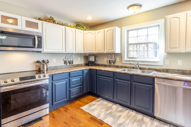 kitchen featuring stainless steel appliances, light wood-type flooring, blue cabinetry, sink, and white cabinets