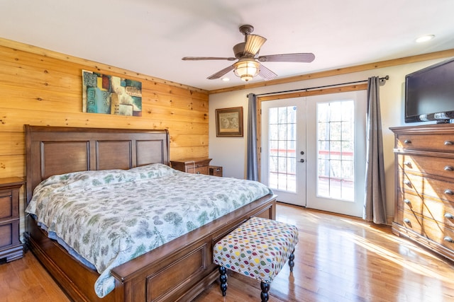 bedroom featuring light hardwood / wood-style floors, ceiling fan, access to exterior, wooden walls, and french doors