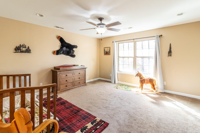 carpeted bedroom featuring a nursery area and ceiling fan