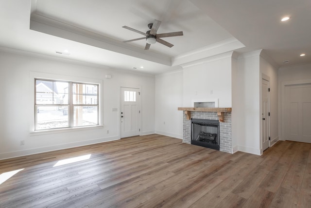 unfurnished living room with crown molding, a tray ceiling, a fireplace, and wood-type flooring