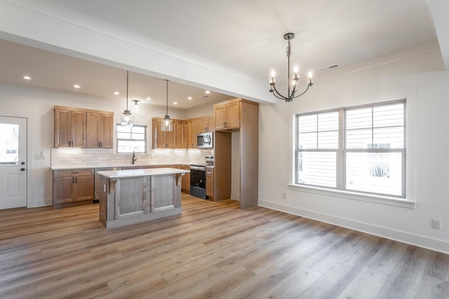 kitchen featuring pendant lighting, backsplash, stainless steel appliances, a center island, and light wood-type flooring