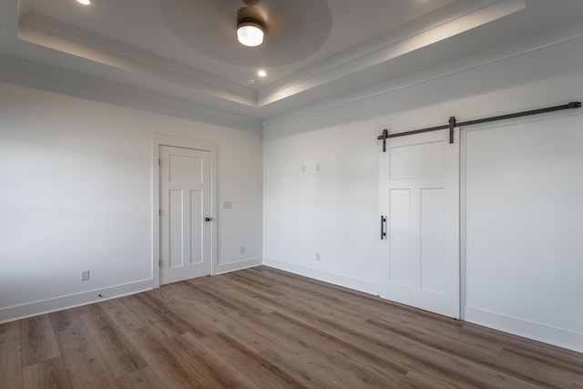 spare room with hardwood / wood-style floors, a raised ceiling, ceiling fan, and a barn door