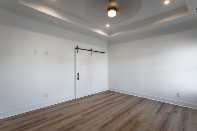 unfurnished bedroom featuring a raised ceiling, a barn door, dark wood-type flooring, and ceiling fan