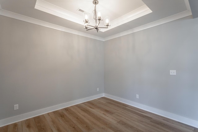 spare room featuring crown molding, a notable chandelier, a tray ceiling, and hardwood / wood-style floors