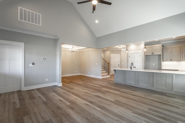 unfurnished living room with ceiling fan with notable chandelier, high vaulted ceiling, sink, and hardwood / wood-style floors