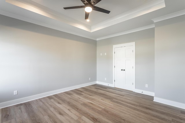 empty room featuring ceiling fan, ornamental molding, a tray ceiling, and hardwood / wood-style floors