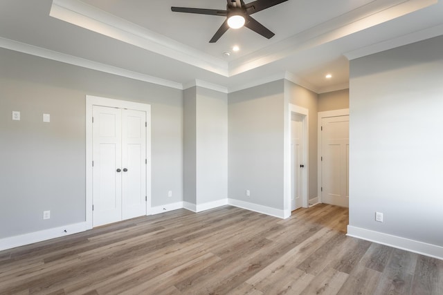 unfurnished bedroom featuring hardwood / wood-style flooring, ceiling fan, a tray ceiling, and crown molding