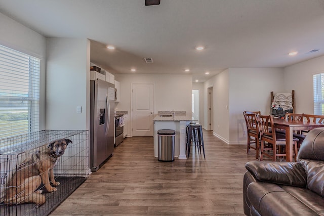 kitchen featuring a kitchen breakfast bar, appliances with stainless steel finishes, white cabinetry, a center island, and light hardwood / wood-style floors