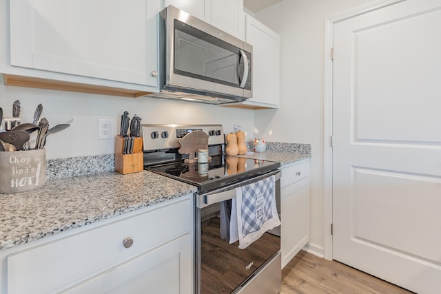 kitchen featuring light stone countertops, white cabinetry, appliances with stainless steel finishes, and light wood-type flooring