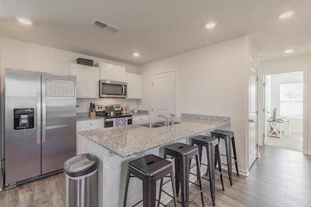 kitchen with light stone countertops, appliances with stainless steel finishes, white cabinetry, sink, and a breakfast bar