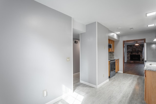 kitchen featuring stainless steel appliances, a fireplace, light wood-type flooring, and tasteful backsplash