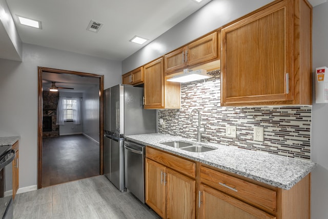 kitchen featuring stainless steel appliances, sink, light stone counters, light wood-type flooring, and decorative backsplash