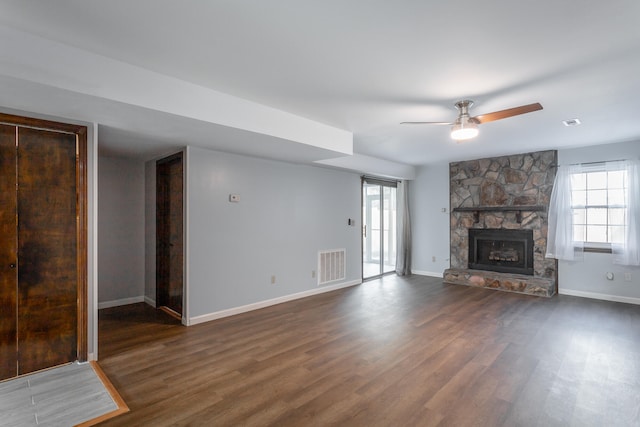 unfurnished living room featuring a stone fireplace, dark hardwood / wood-style flooring, and ceiling fan