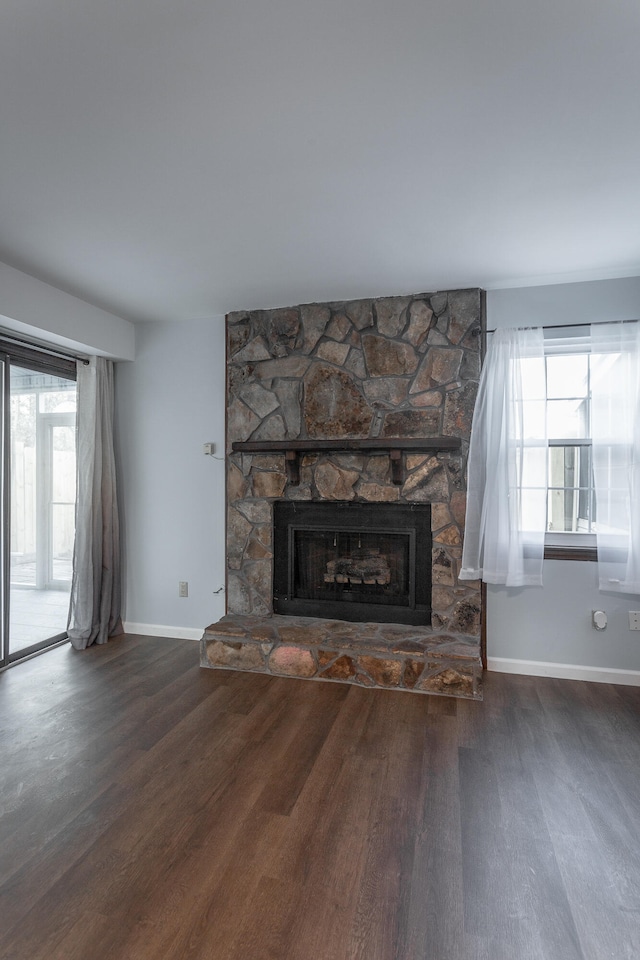 unfurnished living room with a wealth of natural light, a stone fireplace, and dark hardwood / wood-style flooring