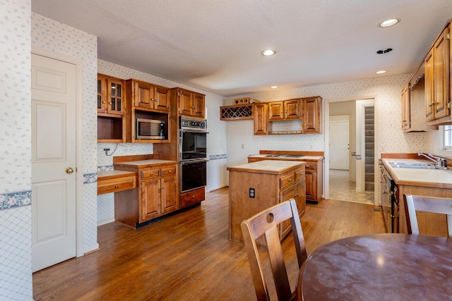 kitchen with sink, dark wood-type flooring, double oven, a center island, and a textured ceiling