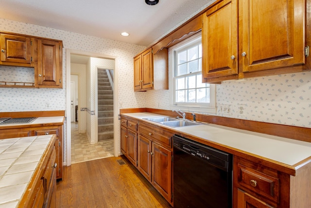 kitchen featuring tile counters, sink, light hardwood / wood-style flooring, and black dishwasher