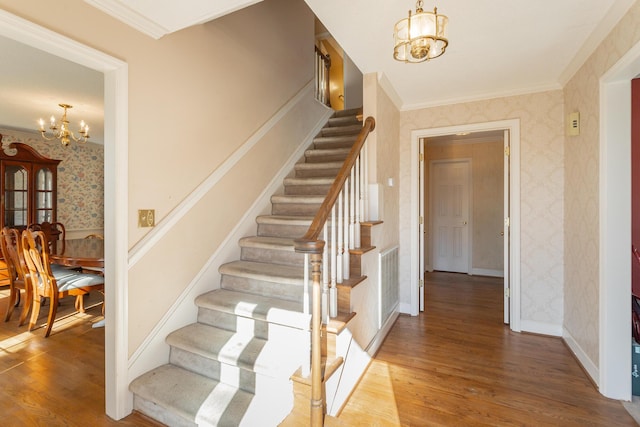 stairs featuring wood-type flooring, crown molding, and a chandelier