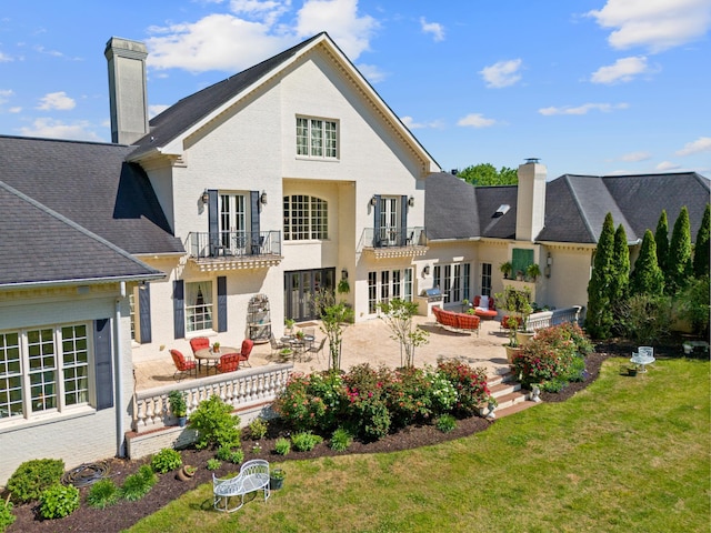 back of property with french doors, a lawn, a balcony, and a patio area