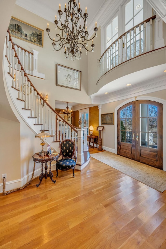 foyer with french doors, hardwood / wood-style floors, decorative columns, crown molding, and a high ceiling