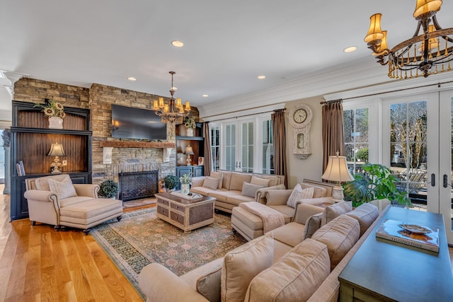 living room with light hardwood / wood-style floors, a stone fireplace, an inviting chandelier, and ornamental molding