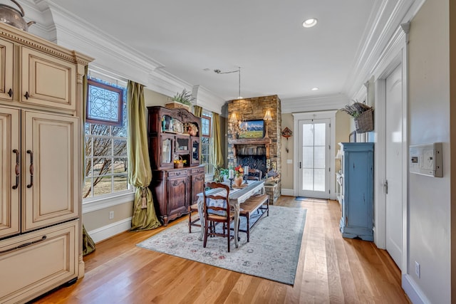 dining space with a stone fireplace, light hardwood / wood-style flooring, and crown molding