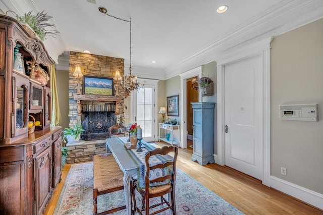 dining space with a stone fireplace, light wood-type flooring, ornamental molding, and a chandelier