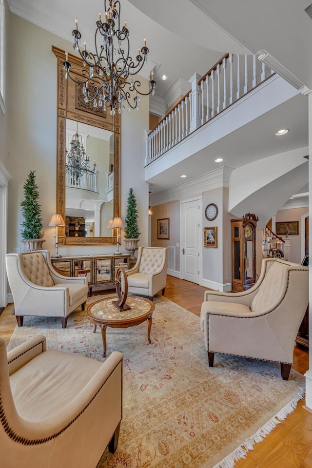 living room featuring light wood-type flooring, a notable chandelier, crown molding, and a towering ceiling