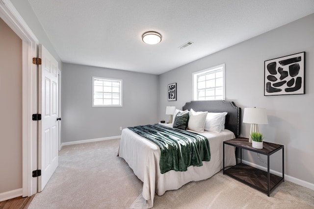 bedroom featuring multiple windows, light colored carpet, and a textured ceiling