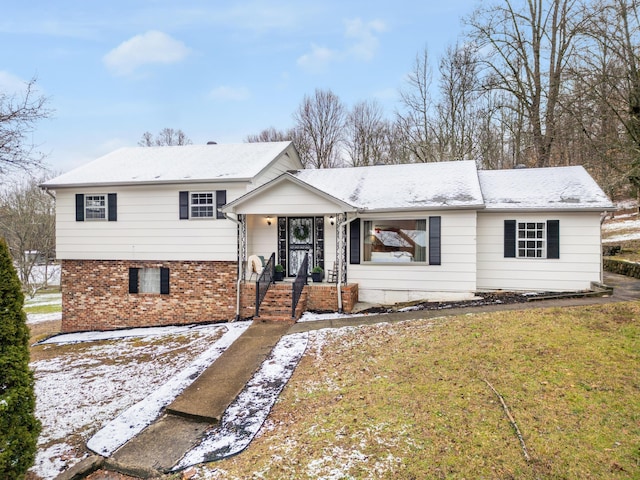 split level home featuring driveway, a porch, a front lawn, and brick siding